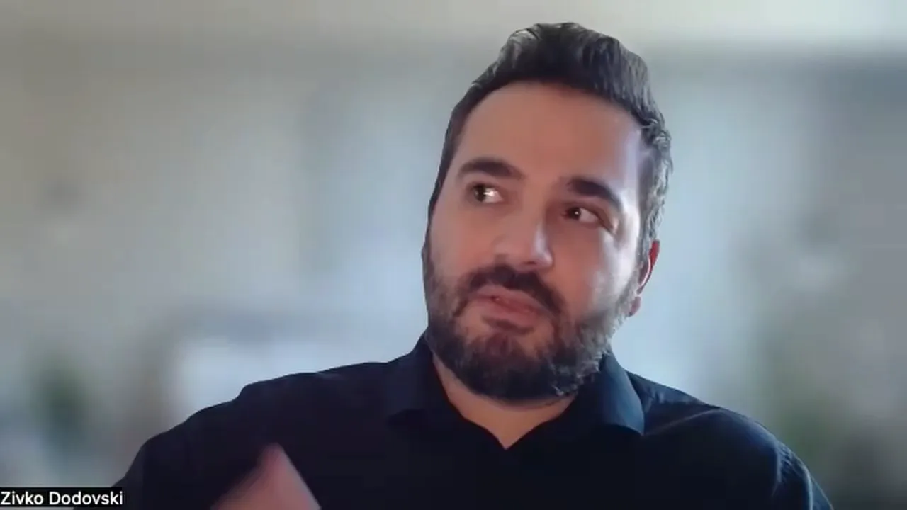 Well‑lit presenter looking up thoughtfully against a softly blurred background, mid-gesture.