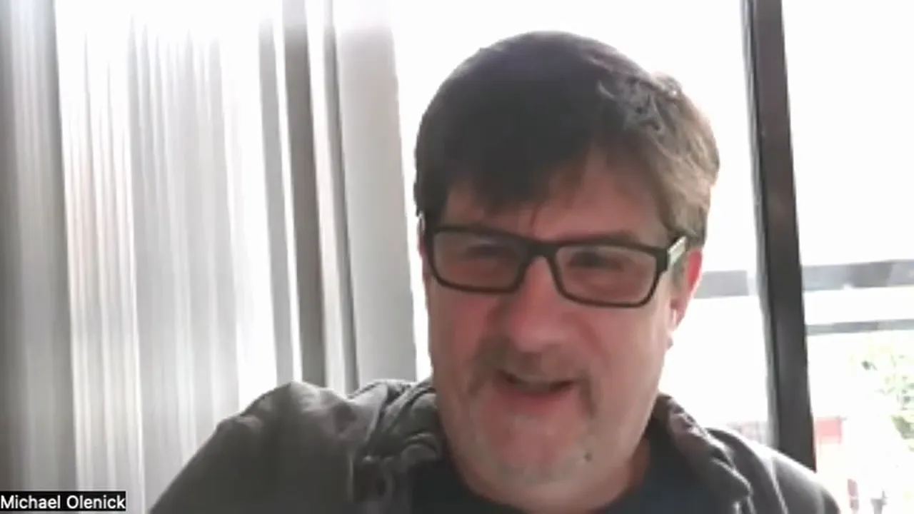 Video-call mid-shot of the presenter speaking, clear face and expression against a bright window background.