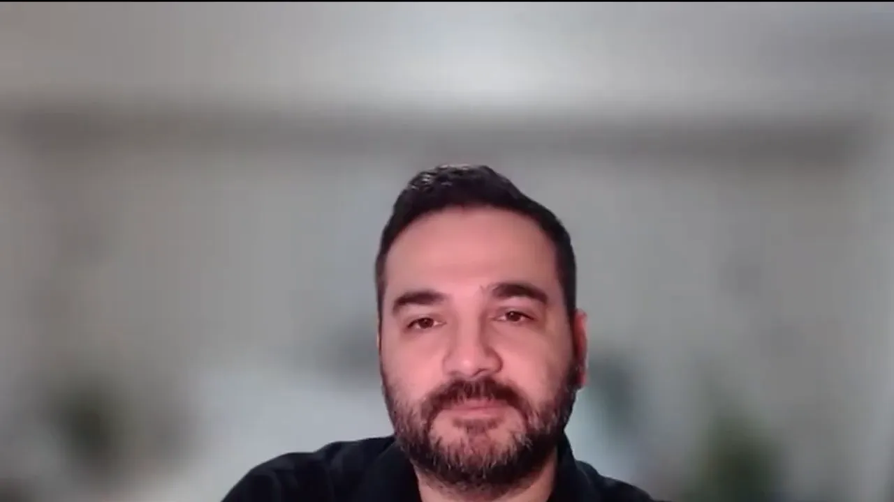 Presenter speaking to camera in a neutral home office background, framed from the shoulders up.