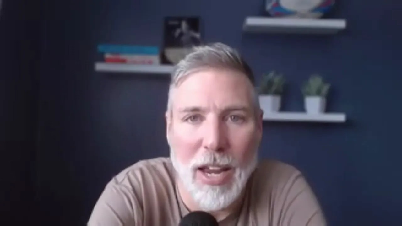 close frontal shot of presenter speaking into a microphone with navy wall and shelves behind