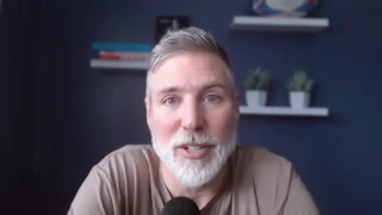 Frontal portrait of host speaking on camera with navy background, shelves and plants visible, microphone in foreground.