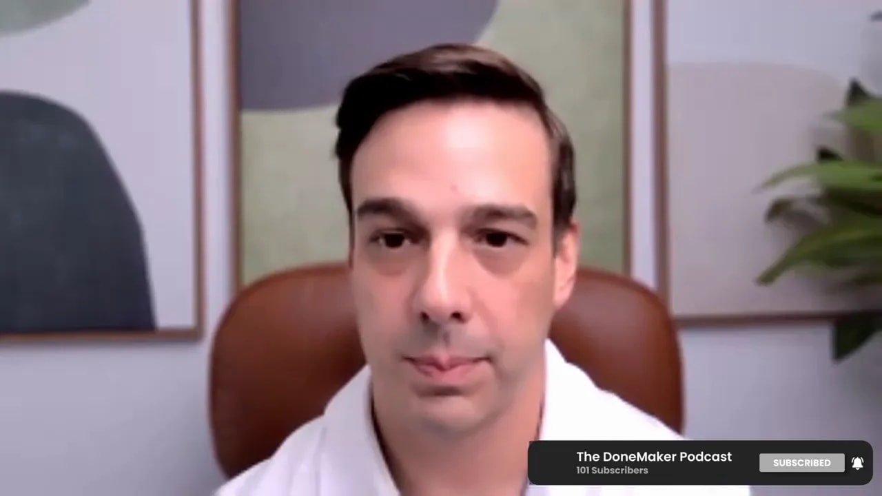 Podcast host on a video call, centered and facing camera with leather chair, framed art and plant behind — clear explanatory shot