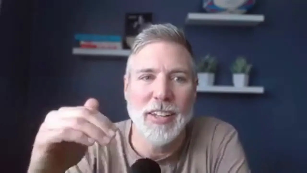 presenter gesturing with hand while speaking, microphone visible, clear facial expression