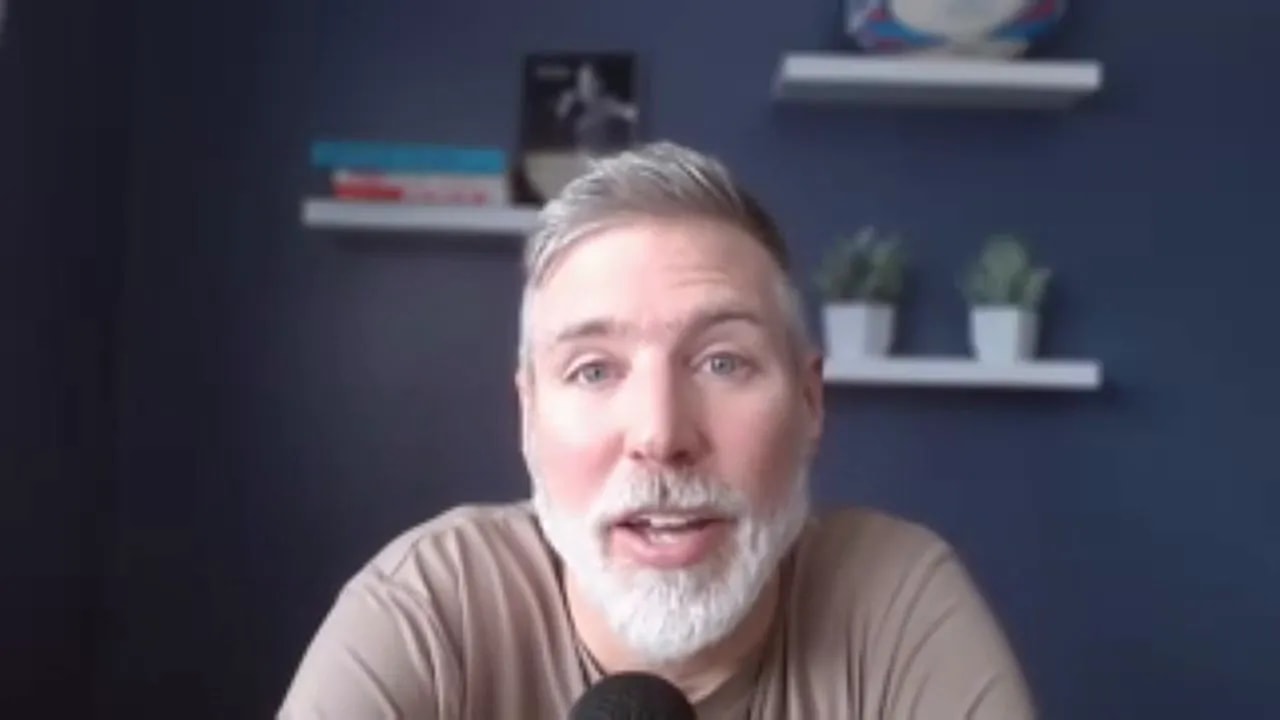 Clear, centered head-and-shoulders shot of host addressing the camera with microphone and navy shelves behind
