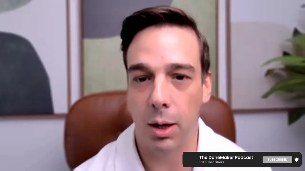 Centered shot of a podcast host speaking on a video call with framed wall art and a plant visible behind them.
