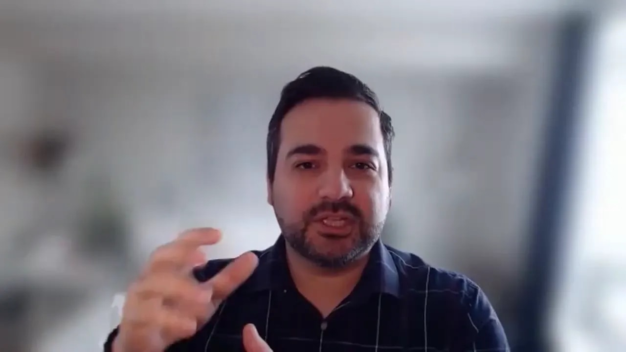 Presenter making a clear hand gesture while explaining a point, with a softly blurred background.