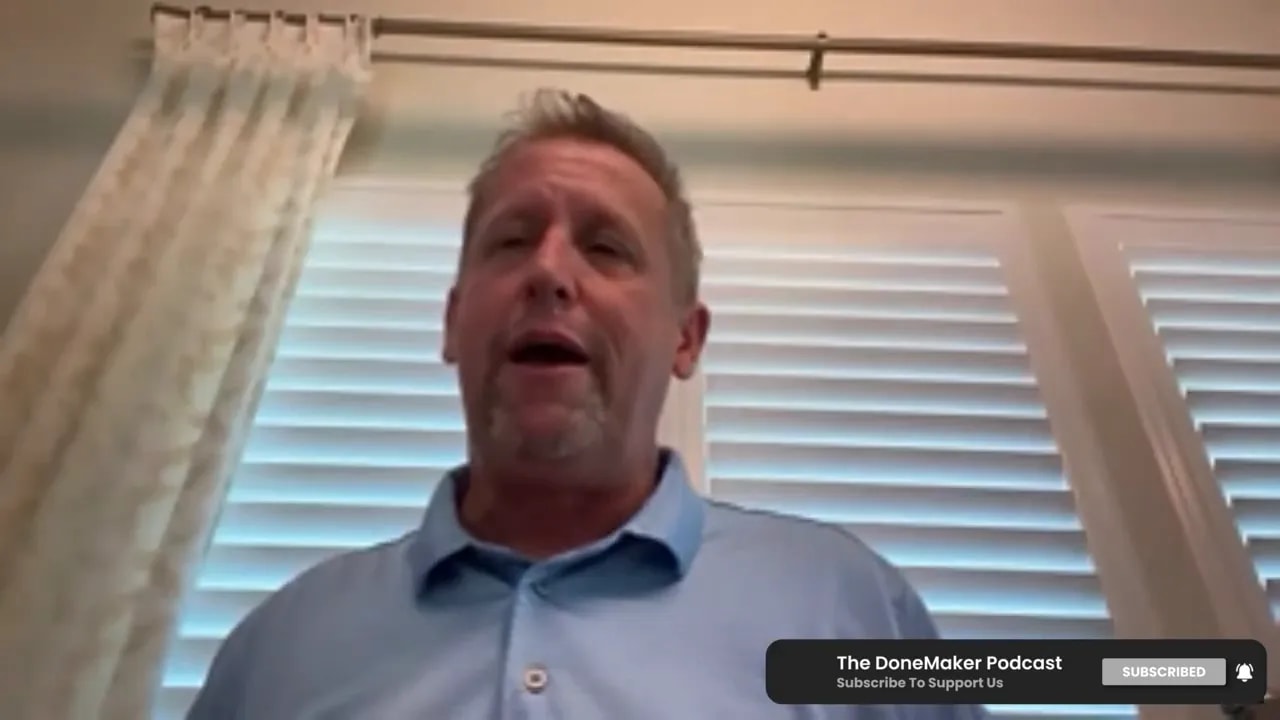 Podcast speaker mid-sentence, framed from the chest up with window blinds and curtain behind him.