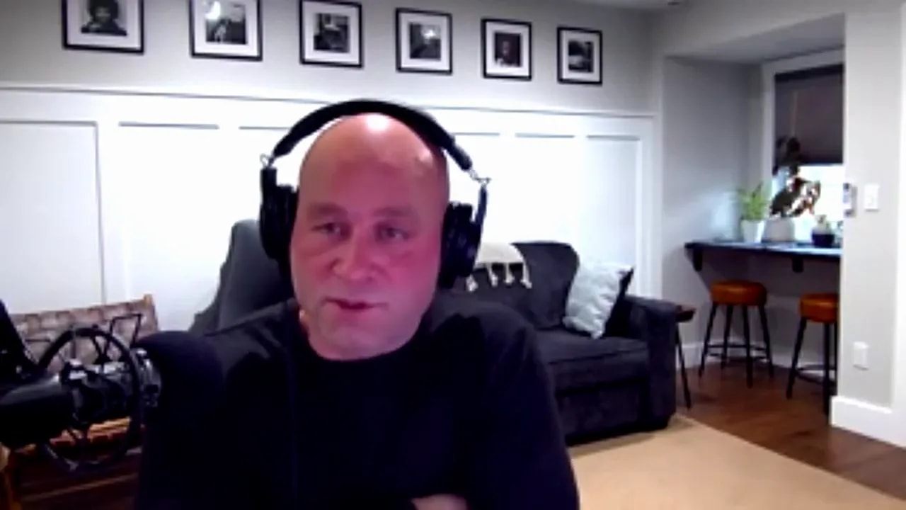 Person on a video call wearing over-ear headphones, speaking into a microphone in a home office setting