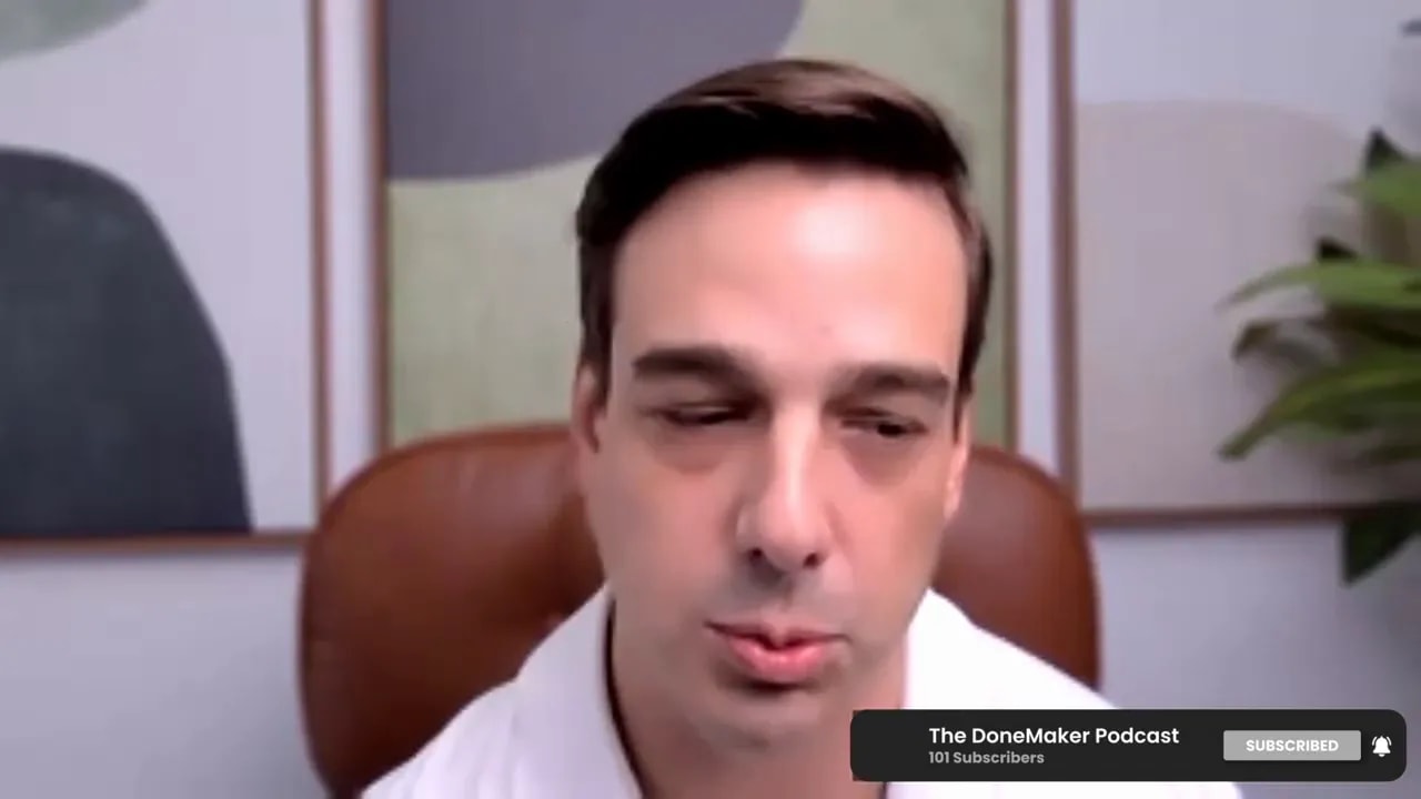 Podcast host on a video call looking downward while explaining financing tradeoffs, with framed art and a plant behind.