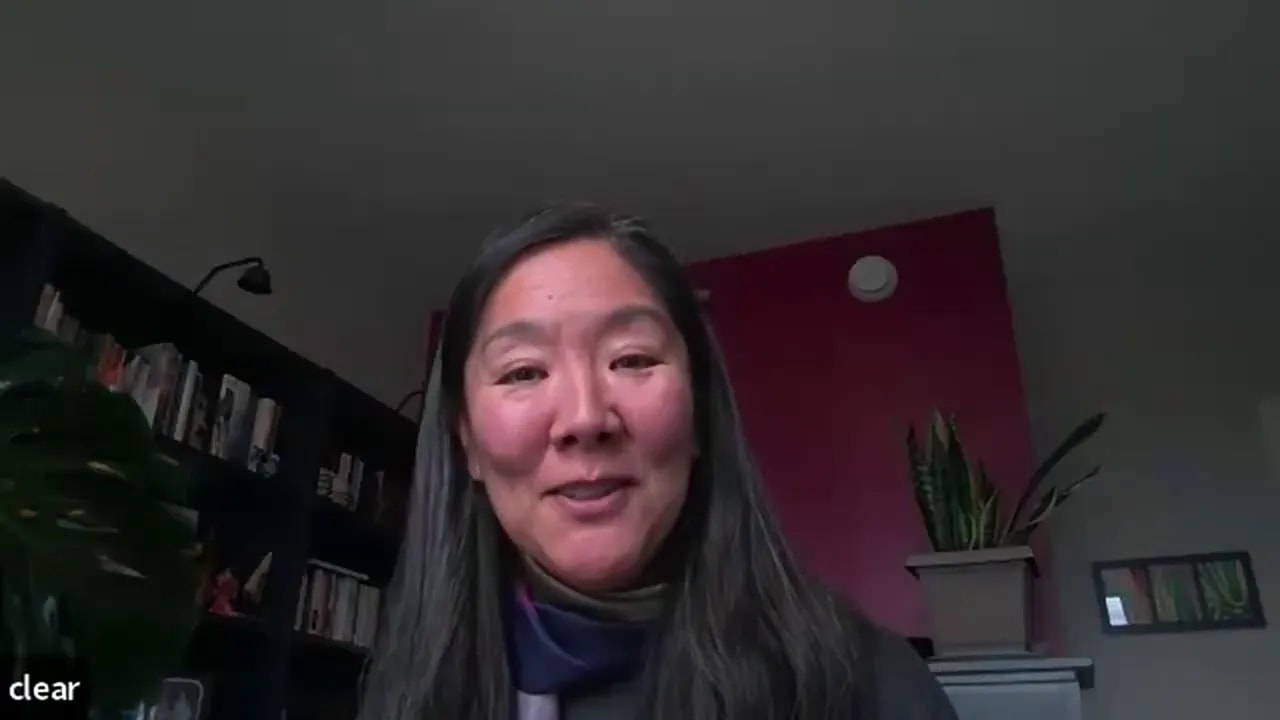 Centered, well-lit leader speaking on a video call in a home office with bookshelves and plants visible