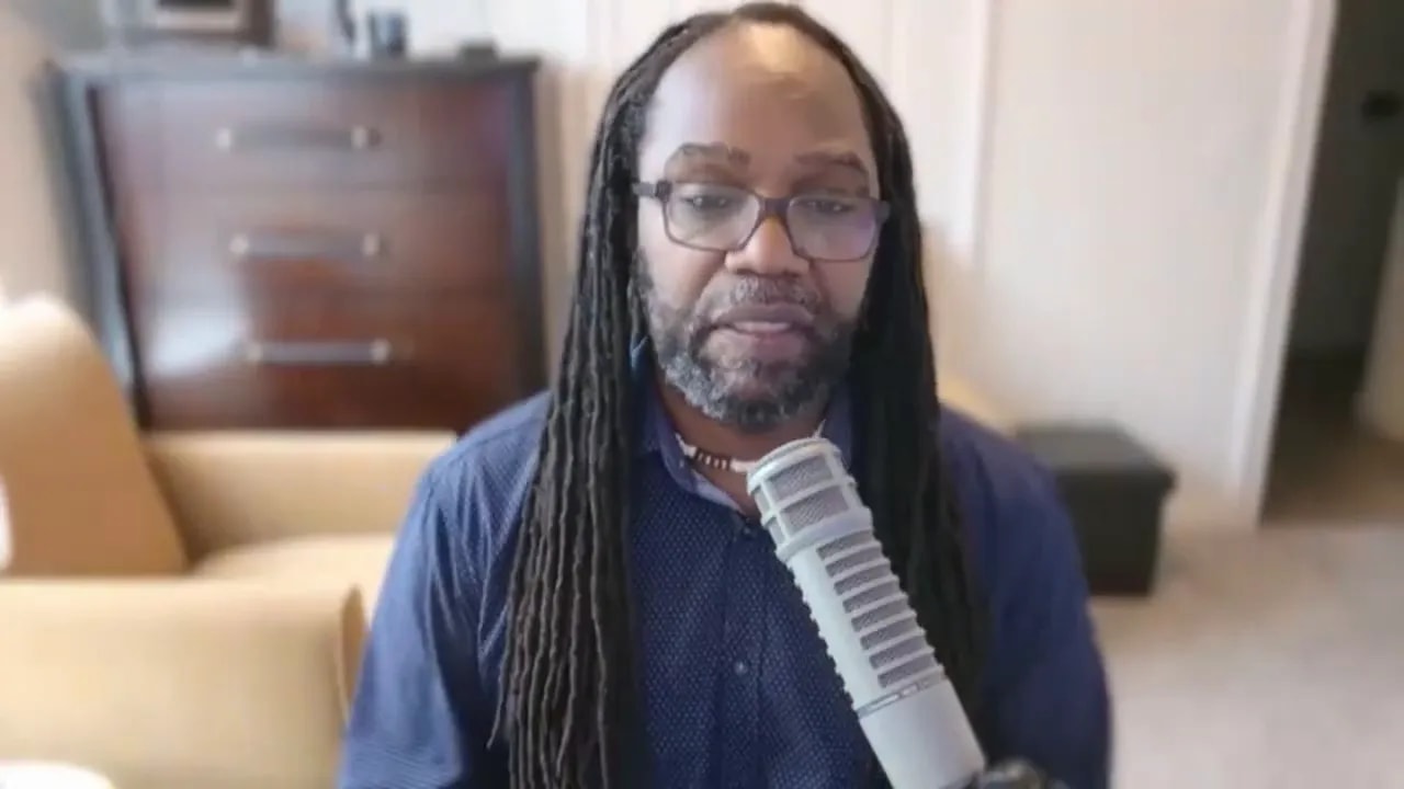 Host speaking into a microphone in a coaching-style video, framed head-and-shoulders