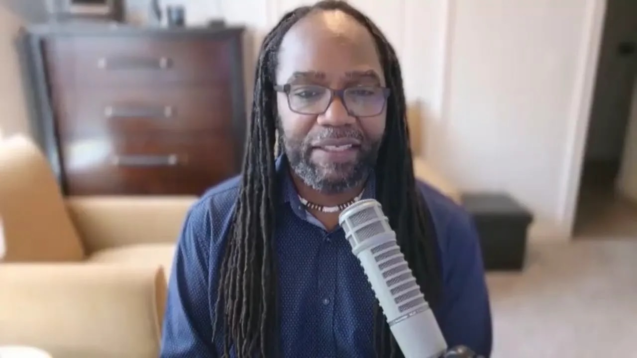 Host speaking into a microphone, head-and-shoulders shot with clear frontal framing