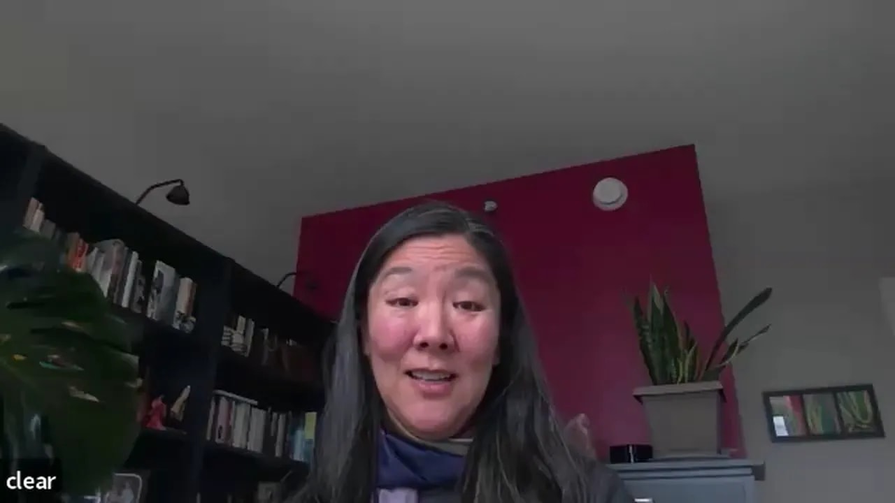 remote leader smiling and speaking on a video call with bookshelf and plant in the background