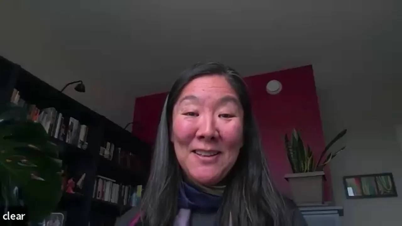 well-lit remote presenter smiling on a video call with bookshelf and plant in the background