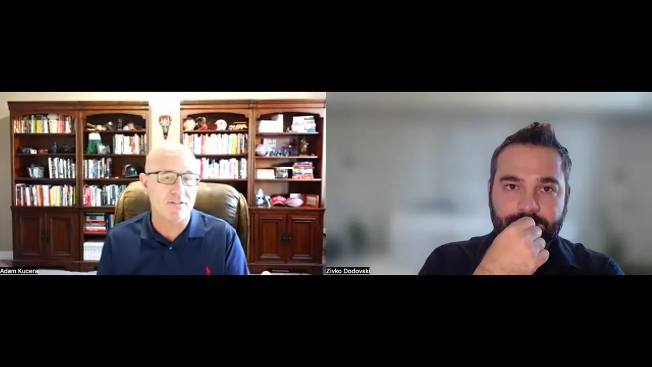 Two people on a video call during a focused meeting; left participant speaking from a bookshelf-lined home office, right participant listening thoughtfully with hand near face and a blurred background.